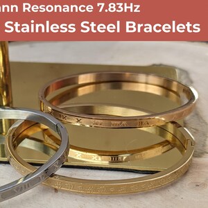 May include: Three stainless steel bracelets with Roman numeral engravings. The bracelets are stacked on top of each other. The top bracelet is rose gold, the middle bracelet is gold, and the bottom bracelet is silver. The text 'Schumann Resonance 7.83Hz' is at the top of the image. The text 'Hight Quality Stainless Steel Bracelets' is below the text 'Schumann Resonance 7.83Hz'.