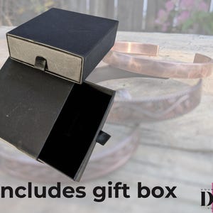 May include: A black gift box with a drawer, open to reveal a black interior. The box is sitting on a wooden surface. Includes gift box.