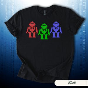 May include: Black t-shirt featuring three colorful robot figures in red, green, and purple. The robots are arranged horizontally across the chest of the shirt. The shirt has short sleeves and a crew neck.