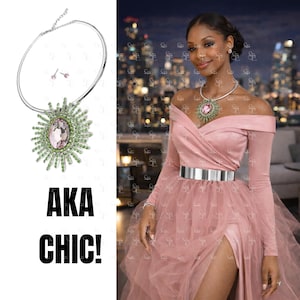 May include: A silver necklace and earrings set with a large pendant featuring a pink gemstone surrounded by green accents. The image also shows a pink off-the-shoulder dress and the text "AKA CHIC!"