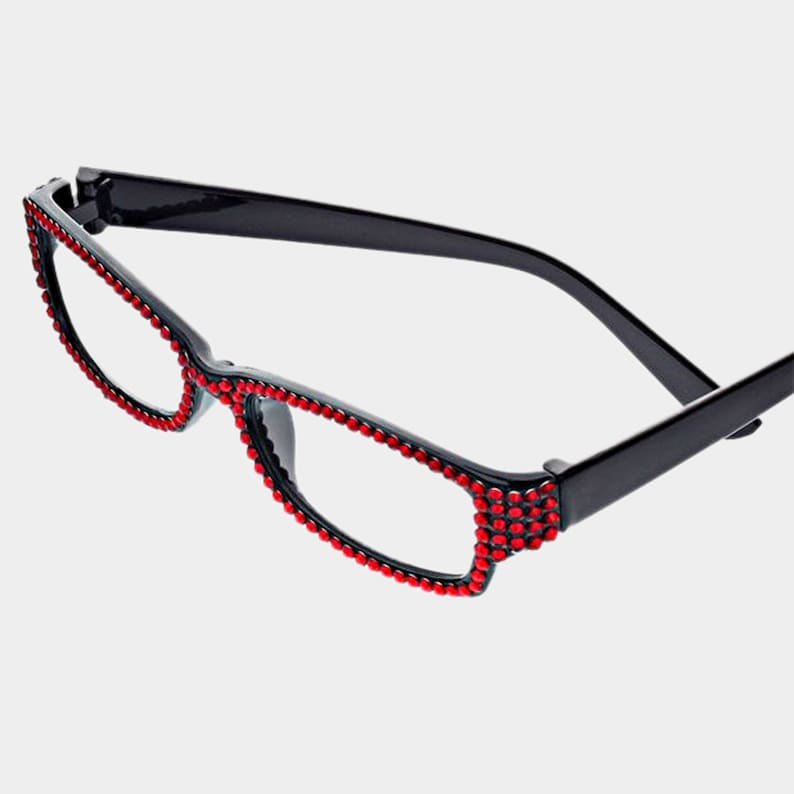 Peut inclure: Lunettes de lecture &agrave; monture noire orn&eacute;es de strass rouges sur les bords. Les lunettes ont une monture demi-cercl&eacute;e et des verres transparents. Les strass ajoutent une touche d'&eacute;clat &agrave; la monture.