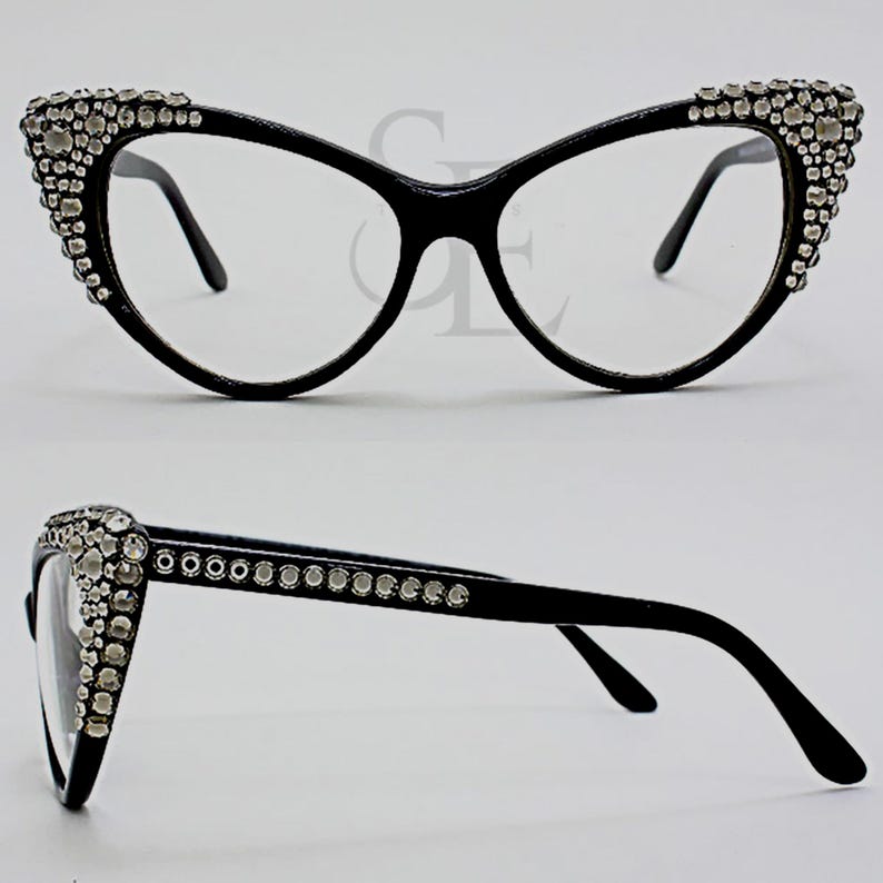 May include: Black cat-eye eyeglasses with clear lenses. The frames are embellished with numerous clear rhinestones along the upper outer edges. The glasses have a sleek, modern design.