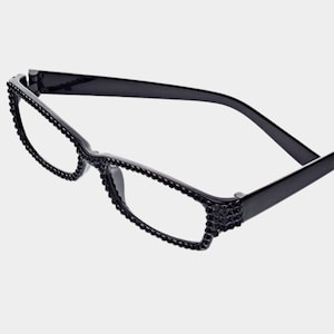 Peut inclure: Lunettes rectangulaires noires avec des verres transparents. Les montures sont orn&eacute;es de petits ornements sombres le long des bords et sur les branches. Les lunettes ont un design classique et &eacute;l&eacute;gant.