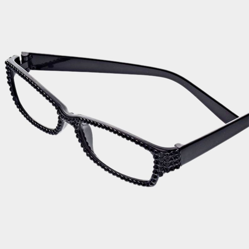 Peut inclure: Lunettes rectangulaires noires avec des verres transparents. Les montures sont orn&eacute;es de petits ornements sombres le long des bords et sur les branches. Les lunettes ont un design classique et &eacute;l&eacute;gant.