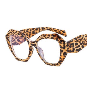 May include: A pair of eyeglasses with a bold, geometric frame. The frame features a leopard print pattern in shades of brown and black. The lenses are clear, and the overall design is modern and stylish.