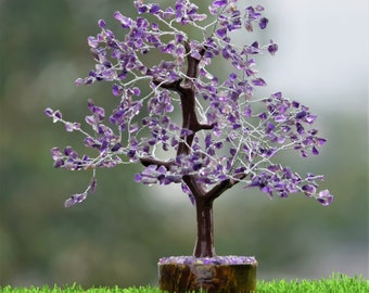 Könnte beinhalten: Eine dekorative Baumskulptur mit einem dunkelbraunen Stamm und Ästen aus gedrehtem, silberfarbenem Draht. Die Äste sind mit zahlreichen kleinen, unregelmäßigen violetten Amethyst-Edelsteinsplittern verziert und der Sockel ist eine runde Holzscheibe.