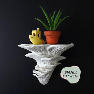 May include: White ceramic mushroom-shaped wall planter with a small yellow toy boat and a potted green plant on top. The planter is 3.9 inches wide.