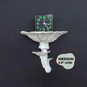 Pode incluir: Prateleira de cerâmica branca em forma de cogumelo com três níveis. Um relógio digital preto com números verdes está sentado no nível superior. A prateleira tem 15 cm de largura.