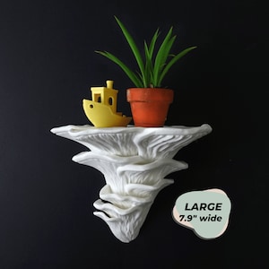 May include: White ceramic mushroom-shaped wall shelf with a yellow toy boat and a small potted plant. The shelf is 7.9 inches wide.