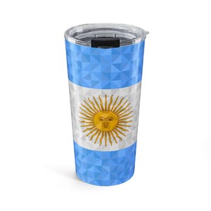 May include: A cylindrical travel tumbler featuring a geometric low-poly pattern in light blue and white, mimicking the flag of Argentina. The center displays a golden yellow sun emblem with a face, also rendered in a faceted geometric style.
