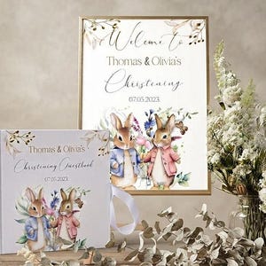 Puede incluir: Un libro de visitas rectangular y un letrero enmarcado a juego con ilustraciones en acuarela de dos conejos con chaqueta. Ambos artículos muestran el texto Welcome to Thomas & Olivia's Christening 07.05.2023 con detalles florales.