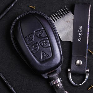 May include: Black leather key fob cover with embossed buttons and a matching key chain. The key chain is stamped with "King Len". A metal tool and screws are also in the image.