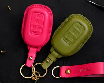 May include: Two leather car key fobs in bright pink and olive green, with gold-colored key rings. The pink fob has a matching wrist strap with the name "Rozalia" embossed. The key fobs have embossed key symbols.