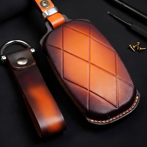 May include: A leather key fob set with a diamond pattern on the key case. The key fob and case are brown and orange with a metal ring and clasp. The key case has a stitched border.