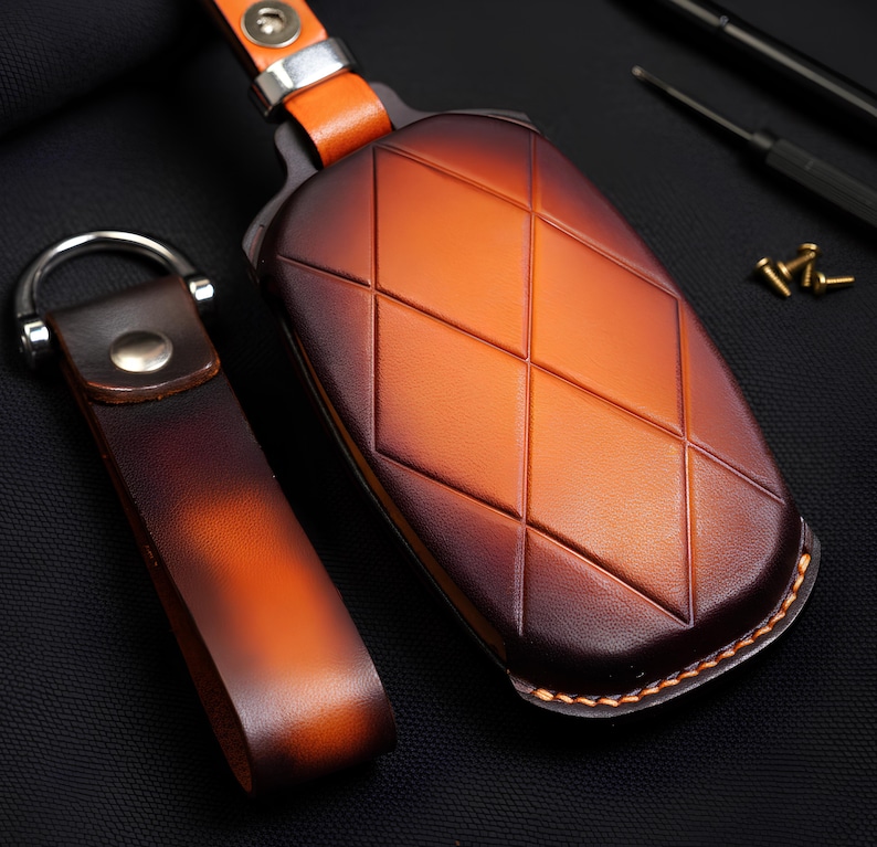 May include: A leather key fob set with a diamond pattern on the key case. The key fob and case are brown and orange with a metal ring and clasp. The key case has a stitched border.