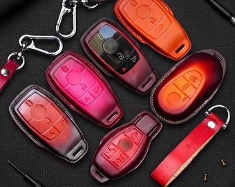 May include: A collection of leather car key fobs in various colors, including red, orange, and burgundy. The fobs are arranged on a dark surface, some with keychains attached. The key fobs have button designs and are likely for car keys.