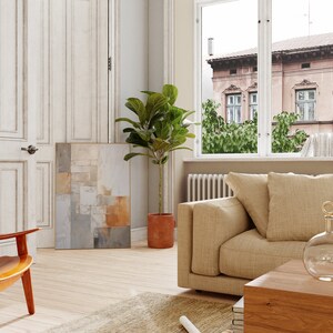 May include: A living room interior with a beige sofa, a potted ficus plant, and a framed abstract painting on the wall. The sofa is positioned in front of a window with a view of a city street.