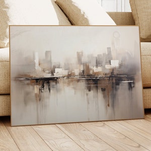 May include: A framed abstract painting of a city skyline in shades of gray, brown, and white. The painting depicts a cityscape with buildings reflected in a body of water.