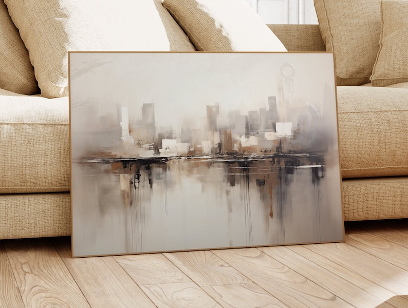 May include: A framed abstract painting of a city skyline in shades of gray, brown, and white. The painting depicts a cityscape with buildings reflected in a body of water.