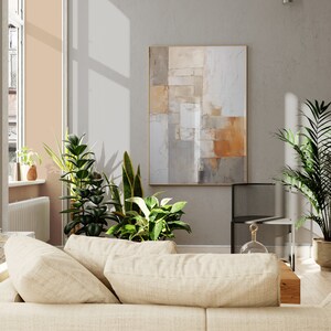 May include: A beige couch with two pillows in a living room with a large abstract painting on the wall, a potted plant, and a black metal chair.