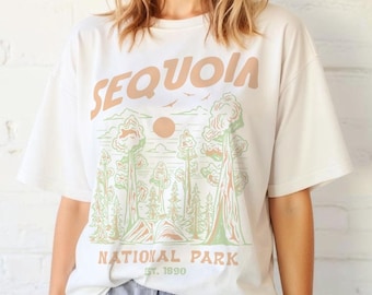 May include: Cream-coloured t-shirt with a Sequoia National Park graphic in brown and green. The shirt features the text "SEQUOIA NATIONAL PARK EST. 1890". Combined with light blue striped shorts.