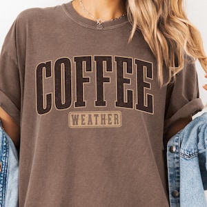 May include: A brown t-shirt with the text "COFFEE WEATHER" in black and brown lettering.