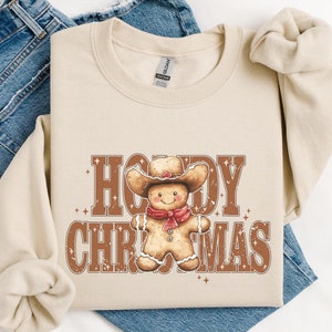 Może przedstawiać: Beżowa bluza z brązowym piernikowym ludzikiem w kowbojskim kapeluszu i napisem "Howdy Christmas".