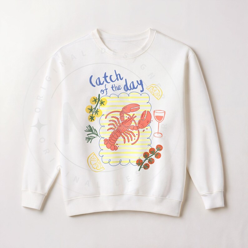 May include: White sweatshirt with a colorful graphic of a lobster, lemon slices, a glass of wine, and the text "Catch of the Day." The design includes yellow and red accents, creating a nautical theme.