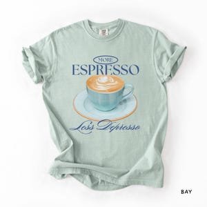 A flat lay of a Bay Comfort Colors shirt with a design featuring an espresso and the phrase More Espresso Less Depresso.