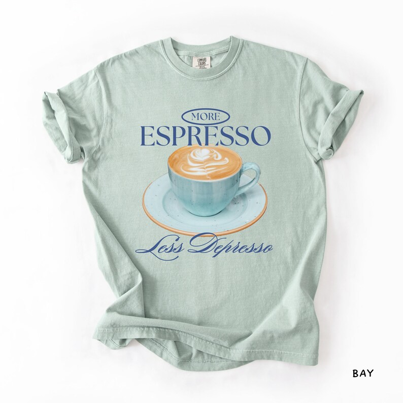 A flat lay of a Bay Comfort Colors shirt with a design featuring an espresso and the phrase More Espresso Less Depresso.