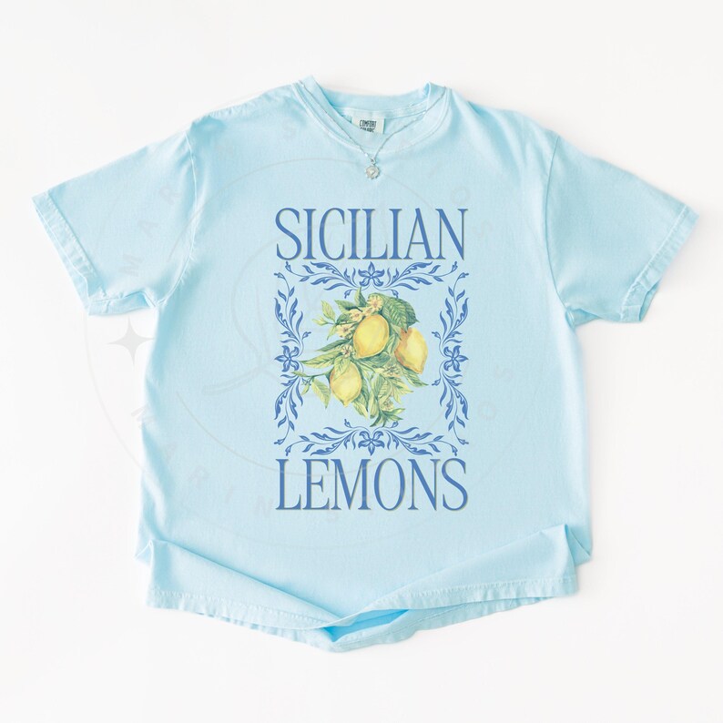 May include: Light blue t-shirt with the words "SICILIAN LEMONS" in blue. The shirt features a floral design with lemons in the center. The shirt has short sleeves and a crew neck.