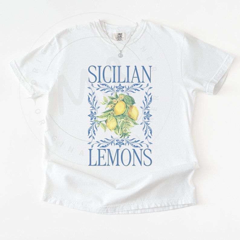 May include: White t-shirt with a blue and yellow graphic. The graphic features the words "SICILIAN LEMONS" in blue, framing a cluster of yellow lemons and green leaves. The shirt has a classic crew neck.