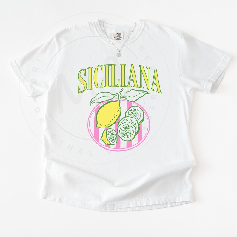 A flat lay of a white Comfort Colors shirt with a design featuring a hand-drawn lemon and lemon slices on a plate, and the phrase Siciliana at the top in a serif font.