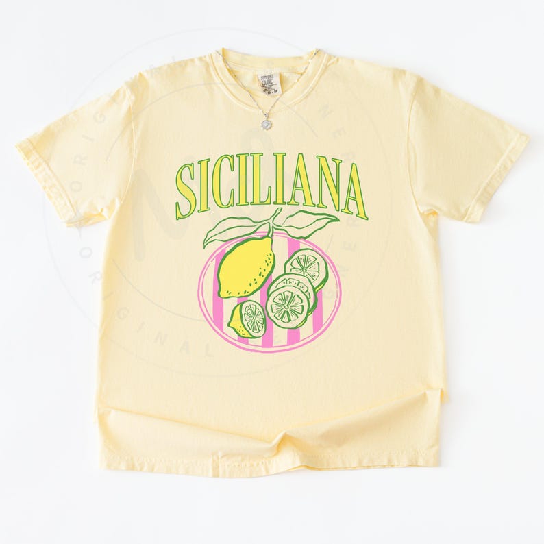 A flat lay of a banana Comfort Colors shirt with a design featuring a hand-drawn lemon and lemon slices on a plate, and the phrase Siciliana at the top in a serif font.
