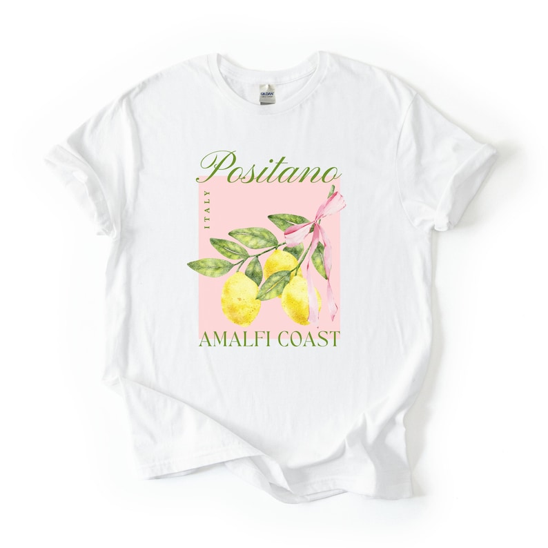 A flat lay of a white Gildan 2000 unisex T-shirt with a design featuring a branch of lemons with a long pink coquette bow tied around it and the phrase Positano, Amalfi Coast, Italy.