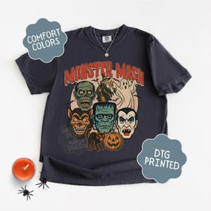 Graphite Comfort Colors Monster Mash Halloween shirt with Frankenstein, Dracula, ghost, witch, and pumpkin retro horror design on a cinnamon-colored oversized tee.