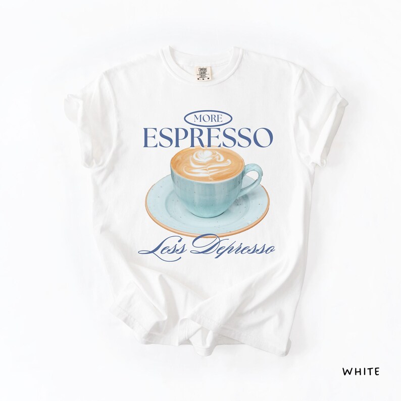 A flat lay of a white Comfort Colors shirt with a design featuring an espresso and the phrase More Espresso Less Depresso.