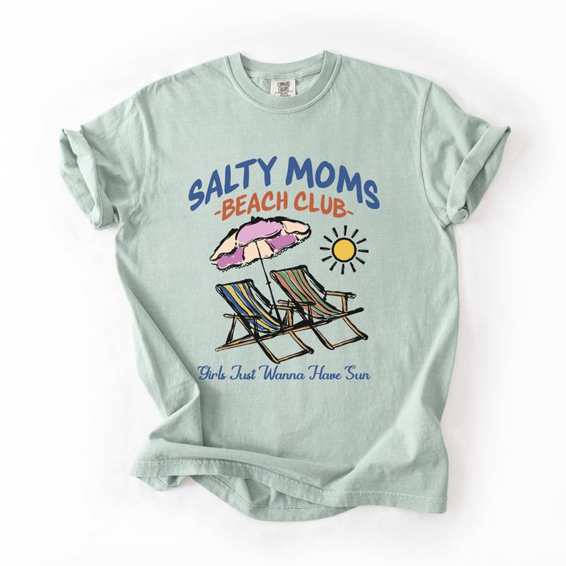 A Bay Comfort Colors shirt ona simple white background with a desgn  featuring a colorful hand-drawn scene of a striped beach umbrella and two chairs with the phrase Salty Moms Beach Club at the top and Girls Just Wanna Have Fun at the bottom of the design.