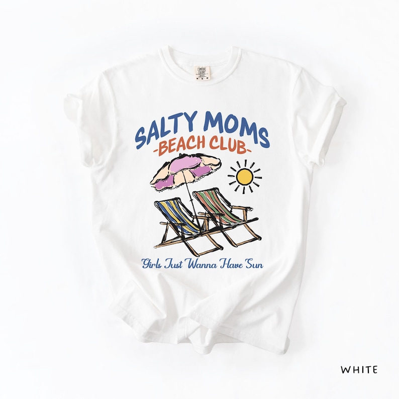 A White Comfort Colors shirt ona simple white background with a desgn  featuring a colorful hand-drawn scene of a striped beach umbrella and two chairs with the phrase Salty Moms Beach Club at the top and Girls Just Wanna Have Fun at the bottom of the design.