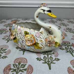 May include: A white ceramic mug with a black handle and the text "But First, Coffee" in a black, handwritten-style font. The mug is on a white surface.