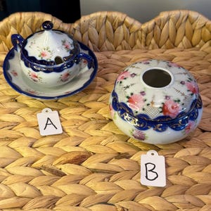 May include: Two porcelain decorative items with floral designs. One is a small sugar bowl with a lid and a saucer, the other is a round container with a lid. Both have blue trim and pink floral patterns. Tags labeled "A" and "B" are in the image.