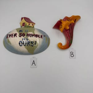 May include: A ceramic wall plaque labeled A featuring a globe with a house and the text BE IT EVER SO HUMBLE IT'S OURS, and a ceramic wall pocket labeled B shaped like a cornucopia with an orange bird and red and orange gradient.
