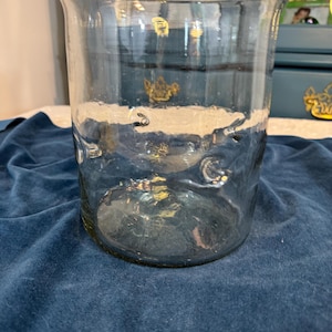 May include: A clear glass vase with a wide, flared top and a rounded base. The vase has a slightly textured surface and is sitting on a dark blue velvet surface. The vase is empty.