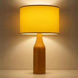 May include: A wooden table lamp with a yellow lampshade. The lampshade is cylindrical with a dark brown trim. The base of the lamp is a light brown colour and has a bottle-like shape. The lamp is turned on, emitting a warm glow.