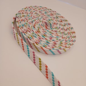 May include: A white fabric ribbon with a colorful polka dot pattern. The ribbon is rolled up and has a diagonal stripe pattern.