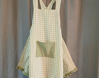 May include: A light green and white checkered apron with a large front pocket. The apron has a ruffled hem and straps that cross in the back. The apron is hanging on a clear plastic hanger.