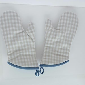 May include: A pair of oven mitts with a beige and white checkered pattern. The mitts have a blue trim and hanging loops. The mitts are designed to protect hands from heat while cooking or baking.