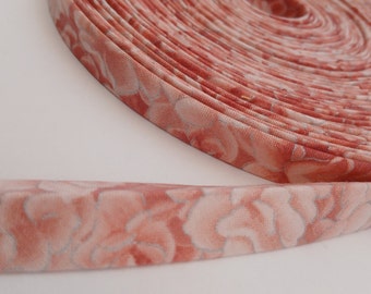 May include: A roll of pink and white floral fabric trim. The trim is rolled up and the fabric is visible. The fabric has a floral pattern with a pink background and white flowers.