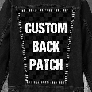 May include: Black denim jacket with a large, rectangular custom back patch. The patch features the words "CUSTOM BACK PATCH" in bold white letters. The jacket has button closures and pockets, and the back patch is stitched onto the jacket.