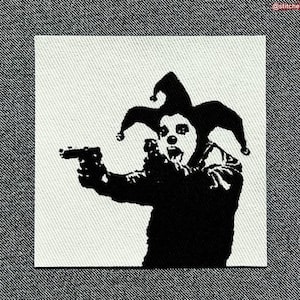 Pode incluir: Patch em preto e branco com um bobo da corte com uma arma. O bobo da corte usa um chapéu com sinos e tem o rosto pintado. O patch é quadrado e colocado sobre um fundo de ganga.